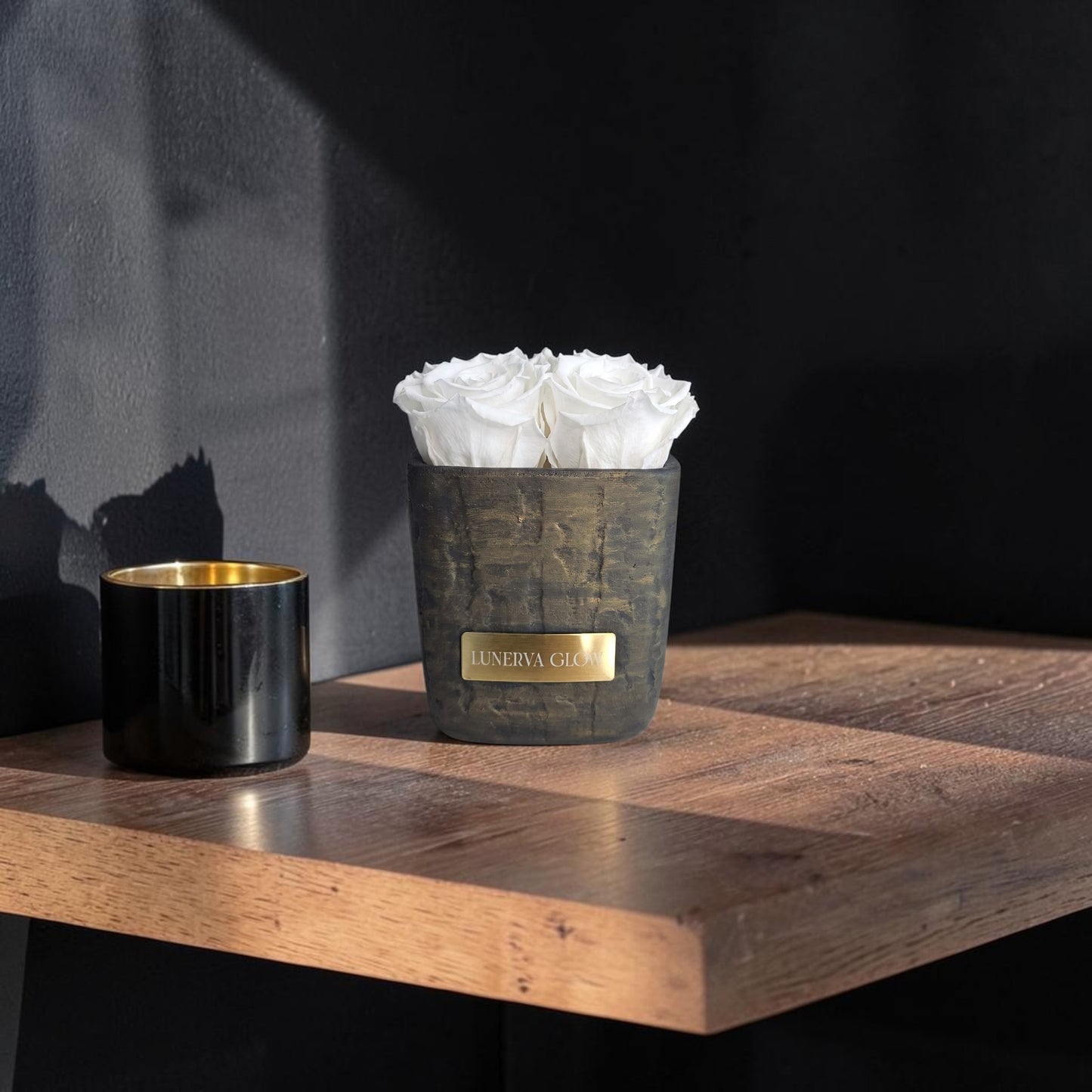 Elegante kleine schwarz-goldene Keramik vase in quadratischer Fo gefullt mit weissen konservierten Rosen.